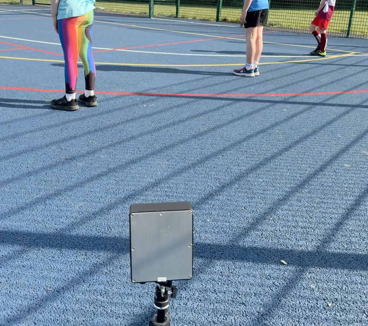 A Sports Vectors radar unit on a tripod at the edge of a school playground, with children on the court in front of it.